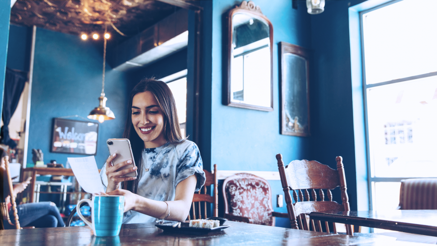 Mulher ao celular em um restaurante, pagando uma conta