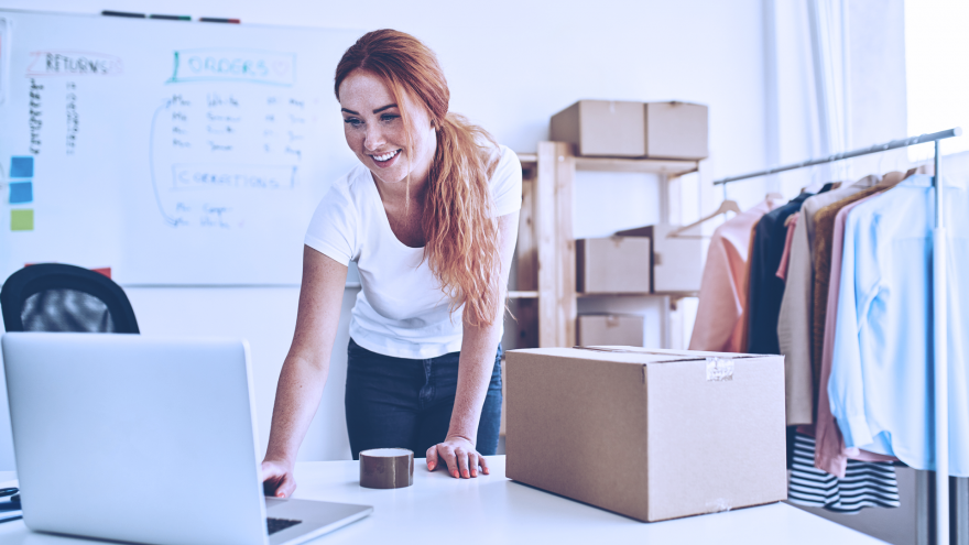 Mulher com computador organizando caixa para envio de compra online